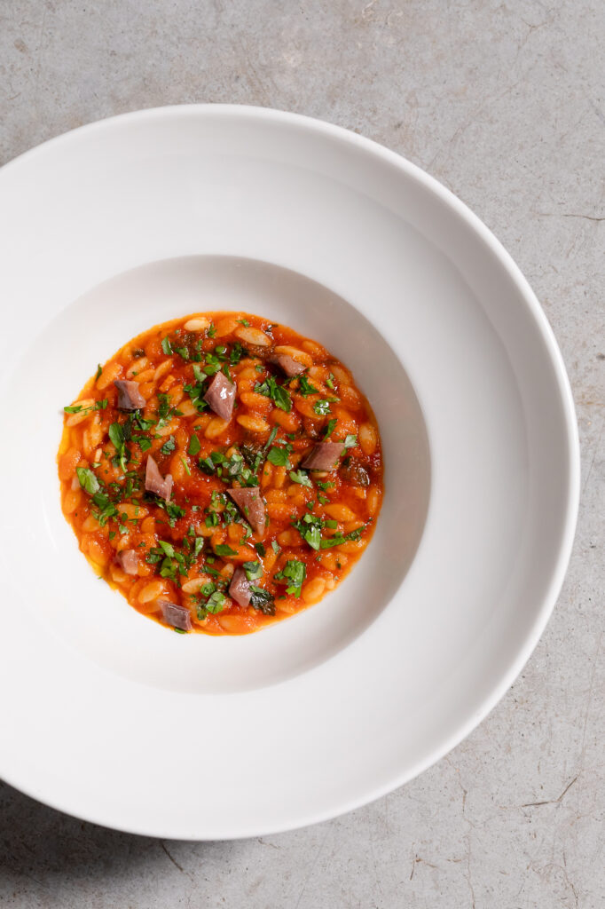 Immagine di un piatto con Chicchi di grano Mancini, salsa di pomodoro, prezzemolo e alici